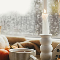 Coffee cup and candle in the window that is rainy