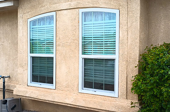 Two windows with white trim and a curved top on a stucco house